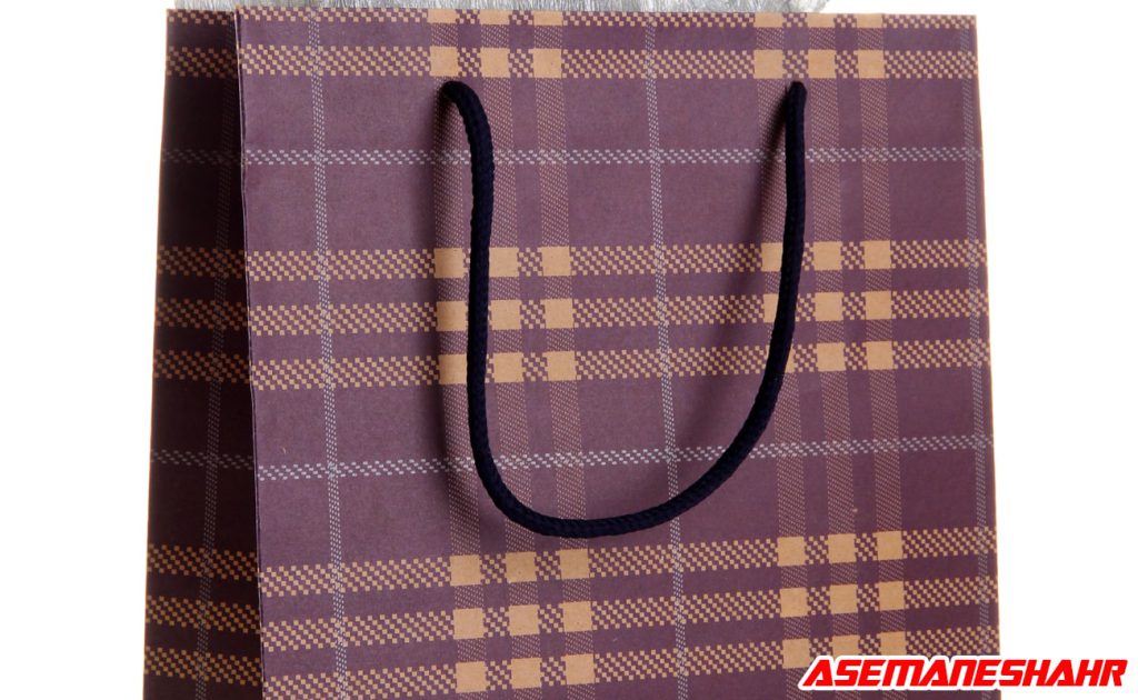 ساک هدیه کاغذی با طراحی چهارخانه کلاسیک به رنگ قهوه‌ ای و زرد، همراه با دسته‌ های کنفی مشکی، مناسب برای بسته‌ بندی شیک هدایا.