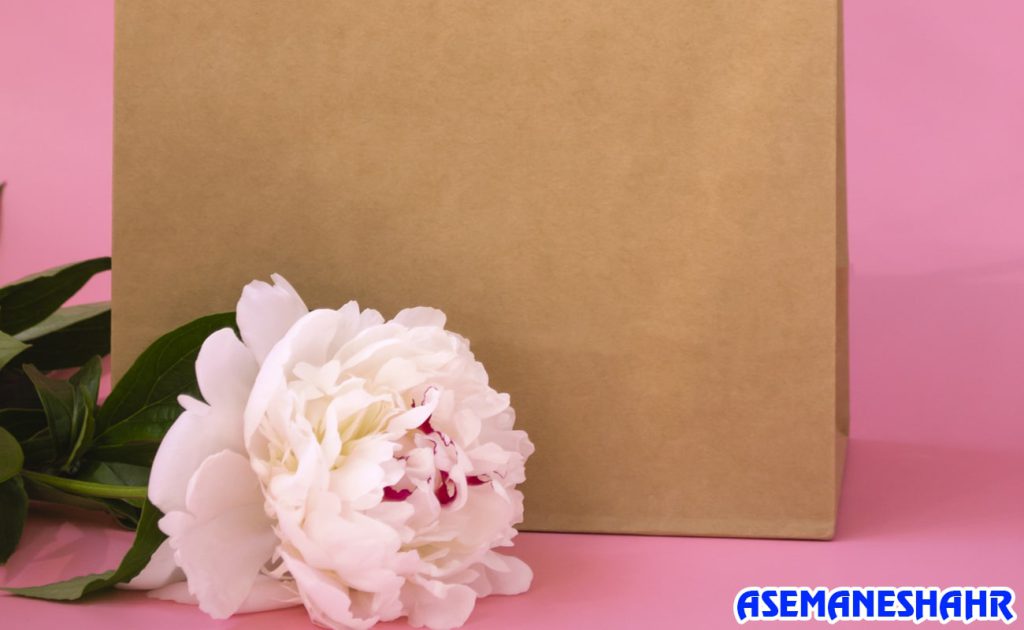 ساک دستی کرافت ساده در کنار گل زیبای پیونی سفید، ترکیبی دلنشین برای هدیه‌ای خاص با طراحی طبیعی و مینیمال.