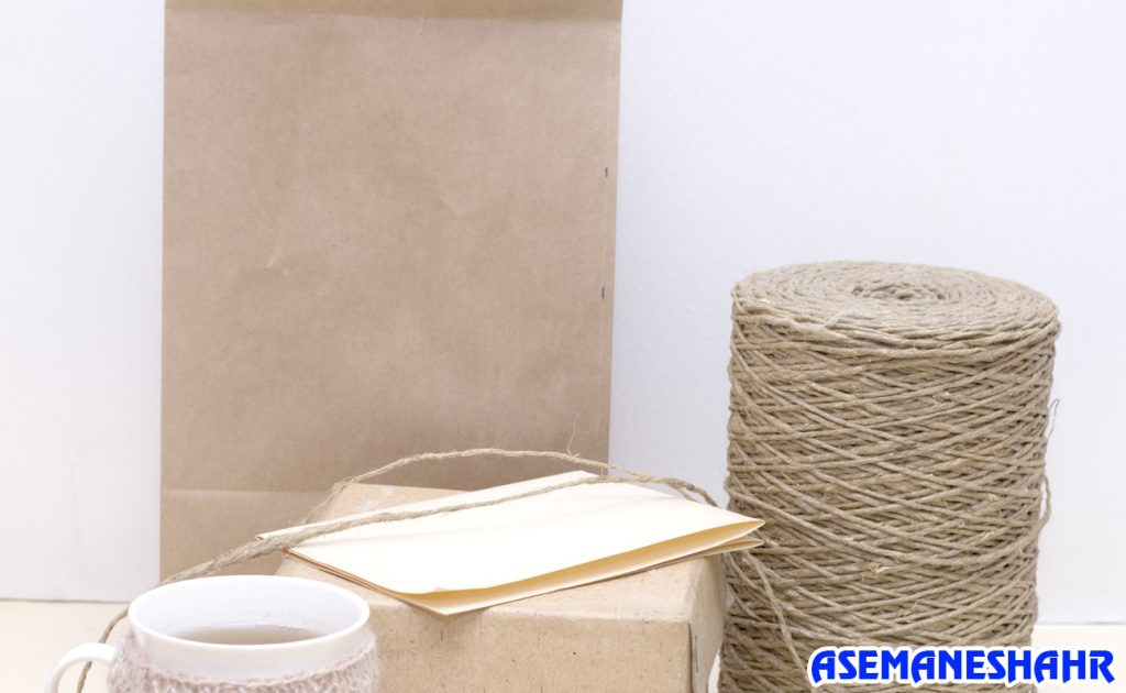 ساک دستی کرافت در کنار نخ کنفی، پاکت کاغذی و یک لیوان چای | مناسب برای بسته‌ بندی طبیعی و هدایا با طراحی مینیمال.