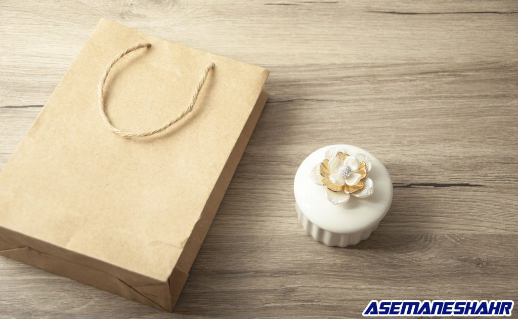 پاکت کادویی کرافت با بند کنفی در کنار جعبه گل دار سفید روی میز چوبی مدرن.