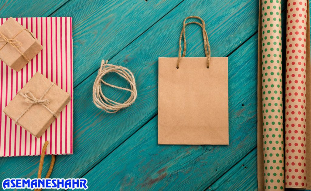 ساک دستی کرافت با بند کنفی و جعبه‌های هدیه، چیدمان خلاقانه برای بسته‌بندی کادو روی زمینه رنگی و شاد.