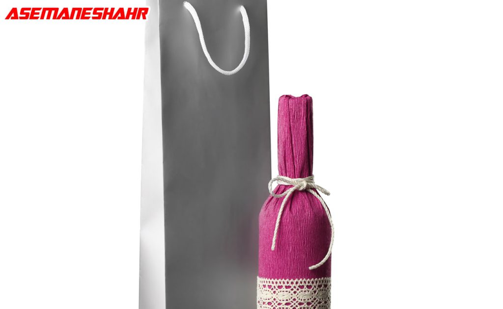 ساک دستی استوانه ای نقره ای زیبا با یک بطری که با تزیینات توری و بسته‌ بندی صورتی.