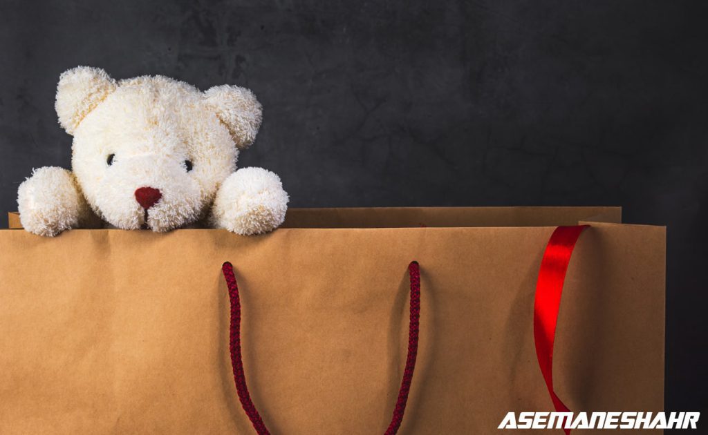 عروسک خرس سفید در پاکت هدیه کاغذی با روبان قرمز.
