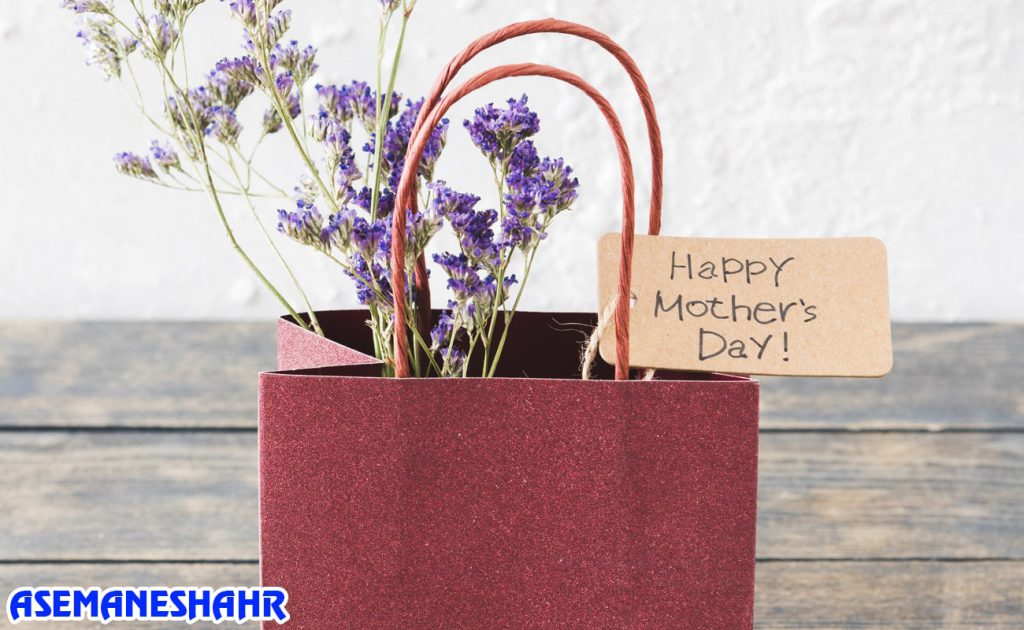 ساک دستی قرمز پر شده با گل‌های بنفش و کارت تبریک روز مادر | انتخابی زیبا و خاص برای قدردانی در مناسبت‌های احساسی.