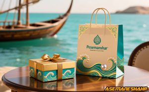 ساک دستی آسمان شهر با طرح موج و مروارید کنار جعبه هدیه طلایی روی میز چوبی در ساحل خلیج فارس با پس‌ زمینه لنج سنتی.