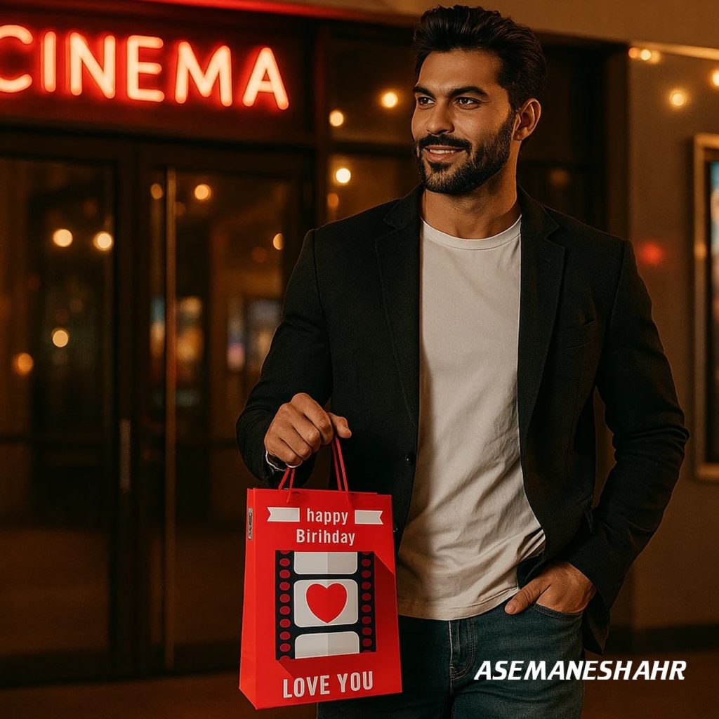 مرد جوان شاد در مقابل سینما با ساک هدیه قرمز آسمان شهر طرح تولد و متن Love You در نور شب.