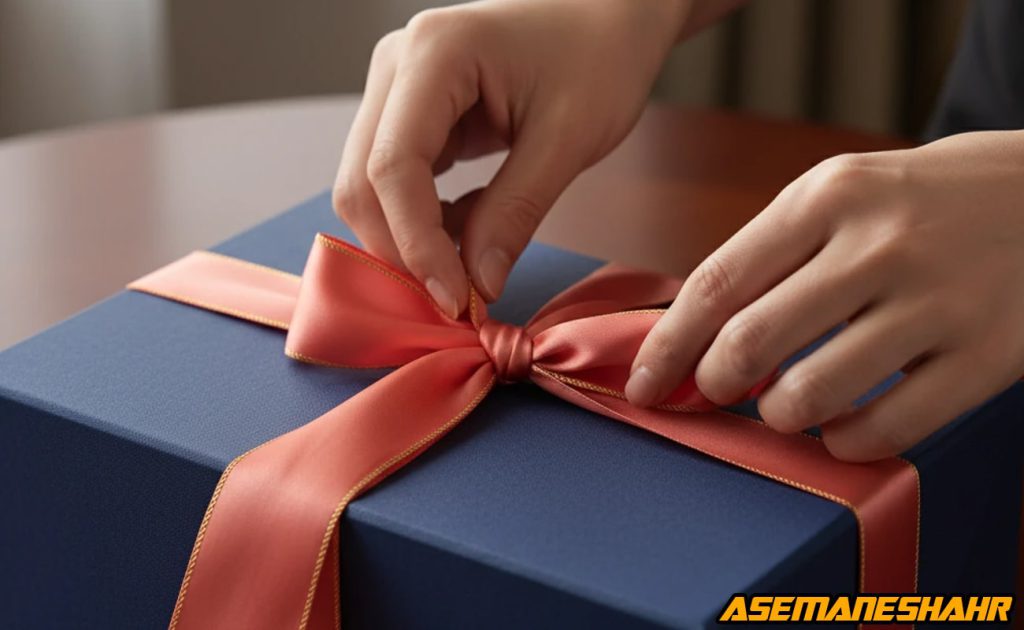 گره زدن روبان مرجانی براق روی جعبه سرمه‌ ای در نور گرم، مرحله نهایی تزئین بسته‌ بندی هدیه آسمان شهر.