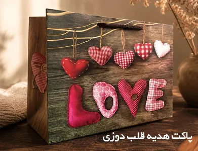 ساک کادوی فانتزی با طرح قلب‌ دوزی پارچه‌ ای و نوشته Love روی پس‌ زمینه چوبی.
