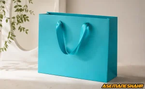 ساک دستی مقوایی فیروزه‌ ای با طراحی مینیمال و بند روبانی براق.